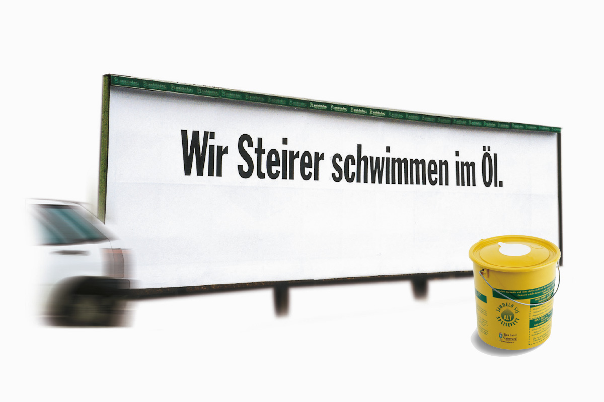Auf dem Bild ist eine Plakatwand mit weißen Hintergrund und der großen schwarzen Aufschrift "Wir Steirer schwimmen im Öl" zu sehen.