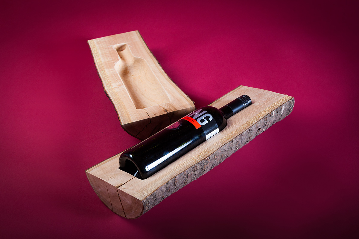 Zu sehen ist eine Weinflasche in einer edlen Holzverpackung auf farbigen Hintergrund. Die Verpackung - der Holzstamm - dient zugleich als Weinkühler.